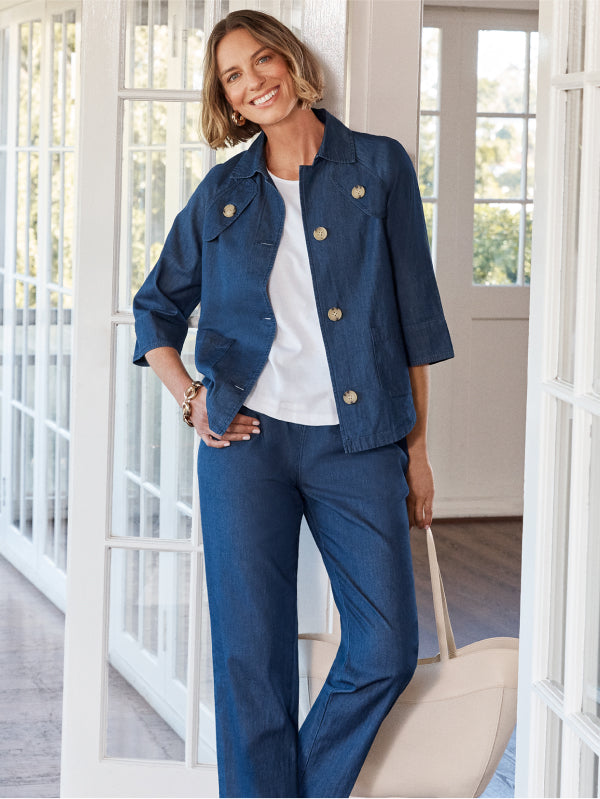 Woman wearing a blue DENIM outfit with large buttons in front of French doors.