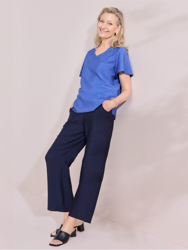 Woman wearing a blue top and navy pants against a plain background