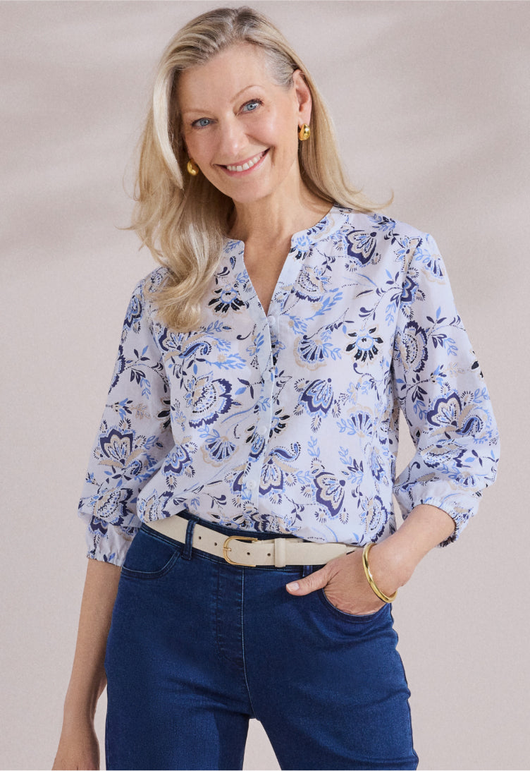 Woman wearing a blue floral blouse and blue jeans against a beige background