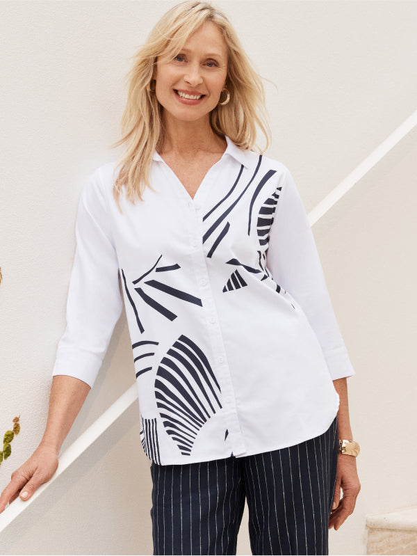 Woman wearing a white shirt with navy abstract patterns and striped pants against a light background