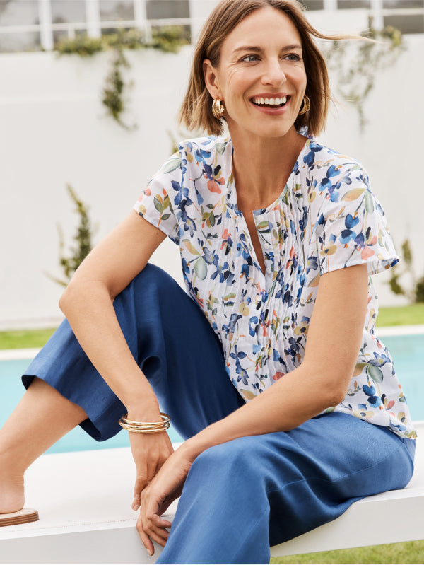 Woman sitting by a pool wearing a floral shirt and blue pants.