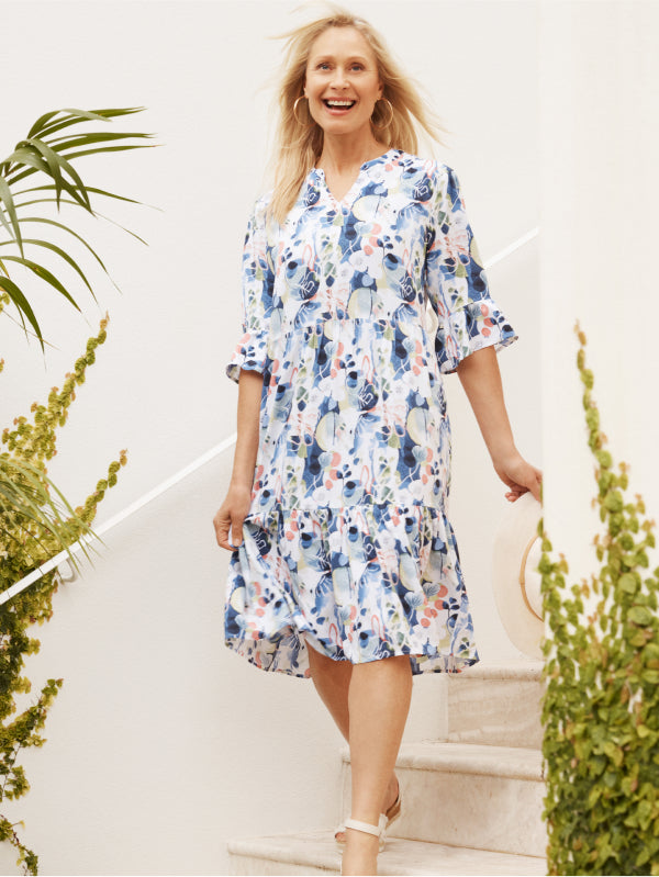 Woman wearing a floral dress standing outdoors with greenery around.