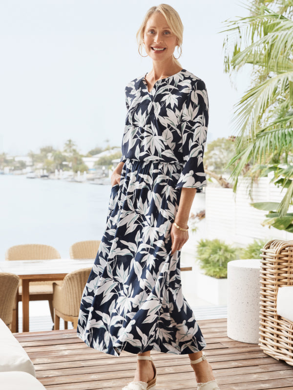 Woman wearing a navy and white floral skirt and shirt standing on a wooden deck with a waterfront background.