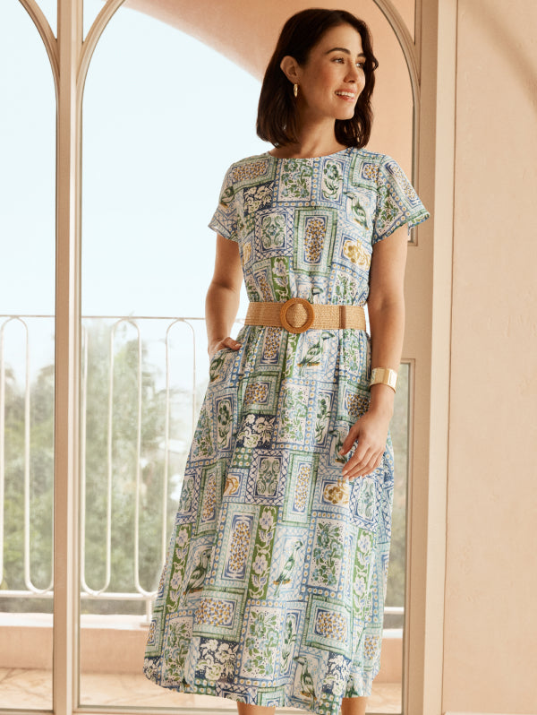Woman wearing a patterned dress standing in a room with large windows.