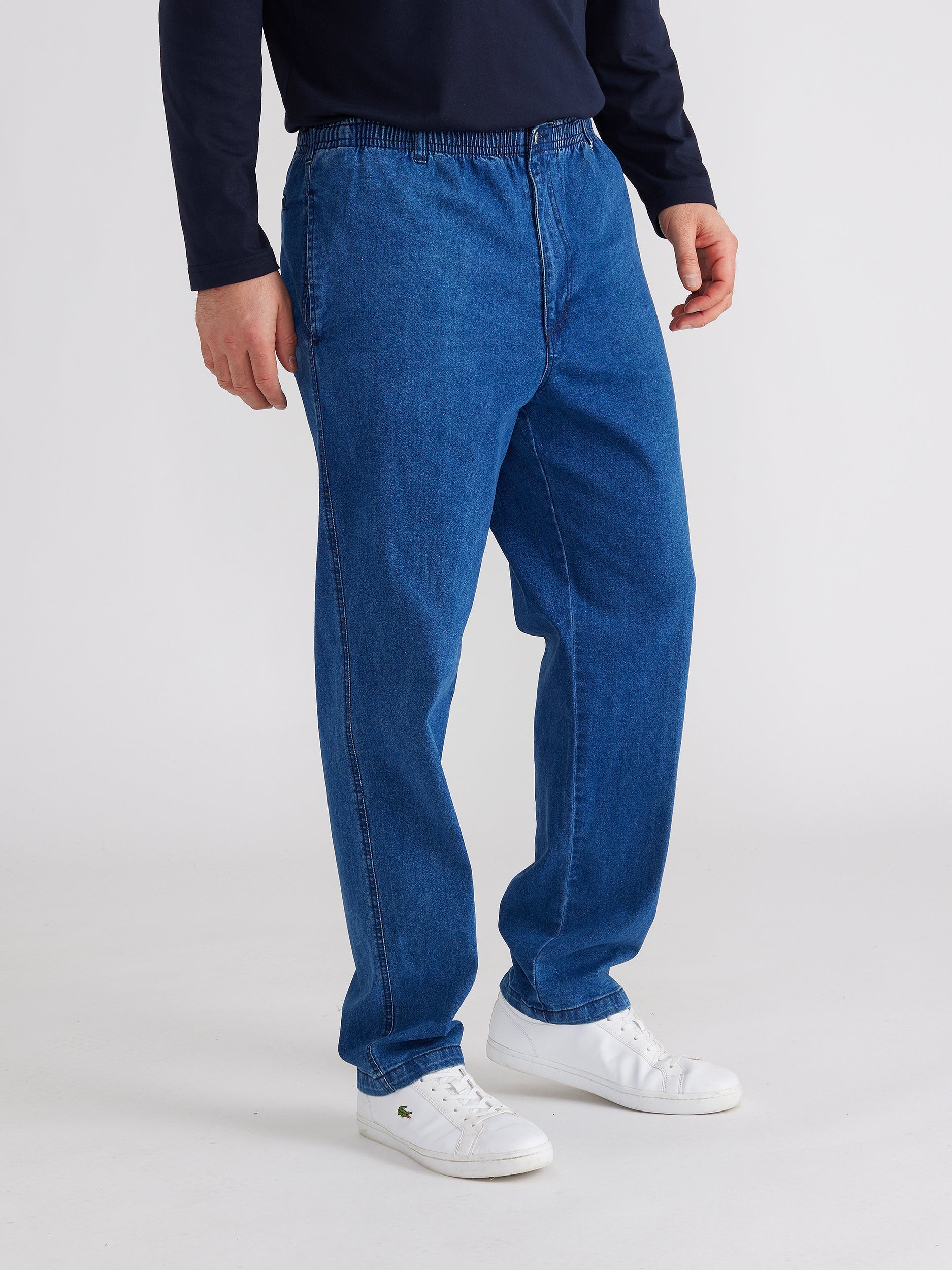 Side image of model wearing mens ipswich denim jean in denim blue colour. The jean has elastic waist and button with fly and side pockets.