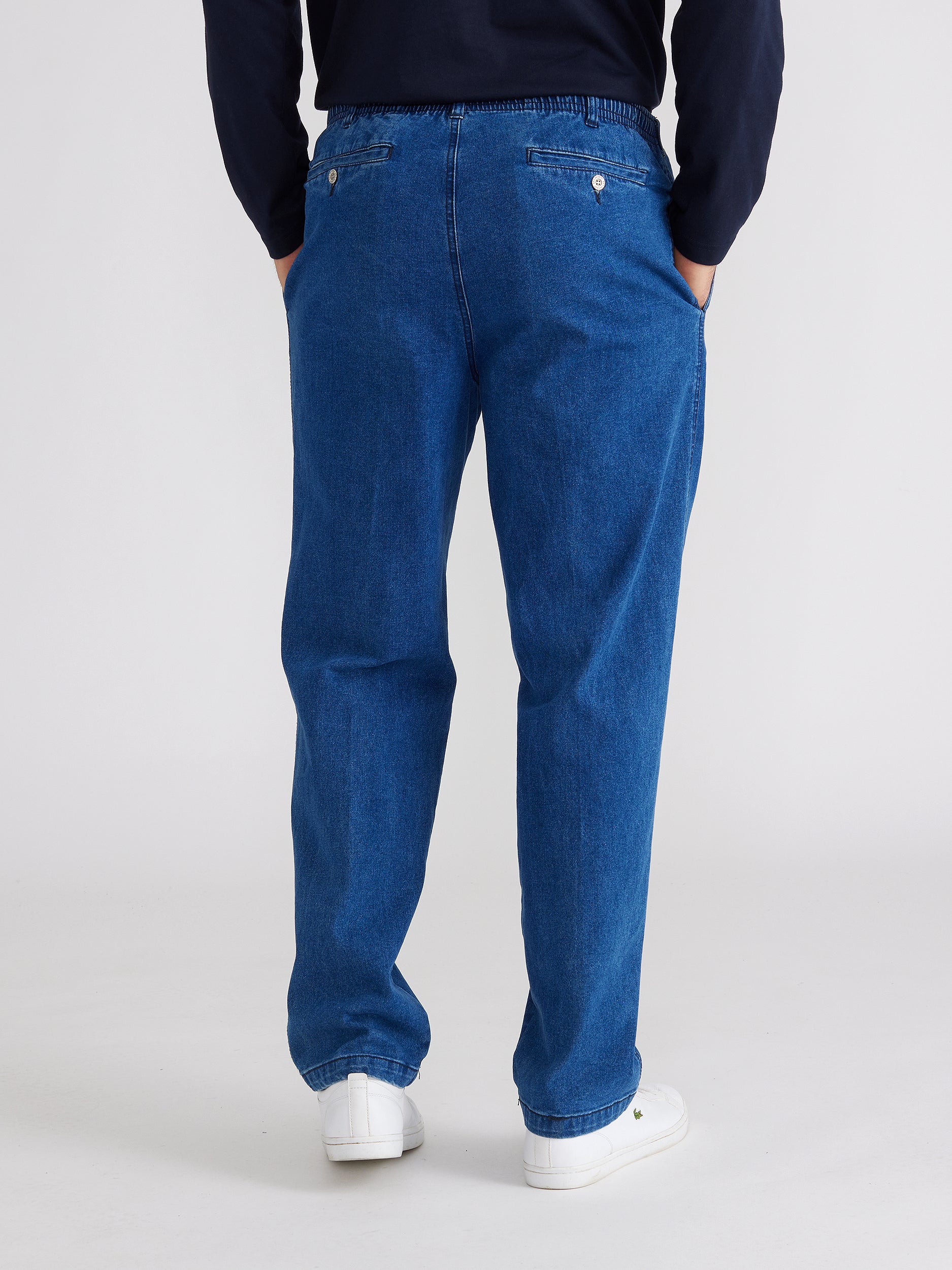 back image of model wearing mens ipswich denim jean in denim blue colour. The jean has elastic waist  and two back pockets. Model has hands in side pockets.
