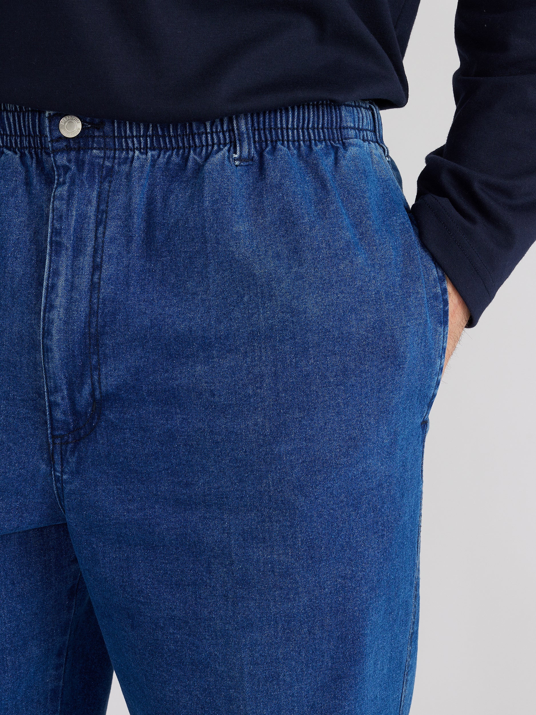 Close up image of model wearing mens ipswich denim jean in denim blue colour. The jean has elastic waist. Model has hand in side pocket.